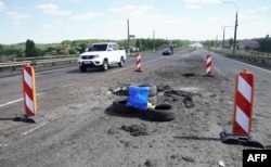 Легковик проїжджає повз воронки від ударів. Антонівський міст у Херсоні, 21 липня 2022 року