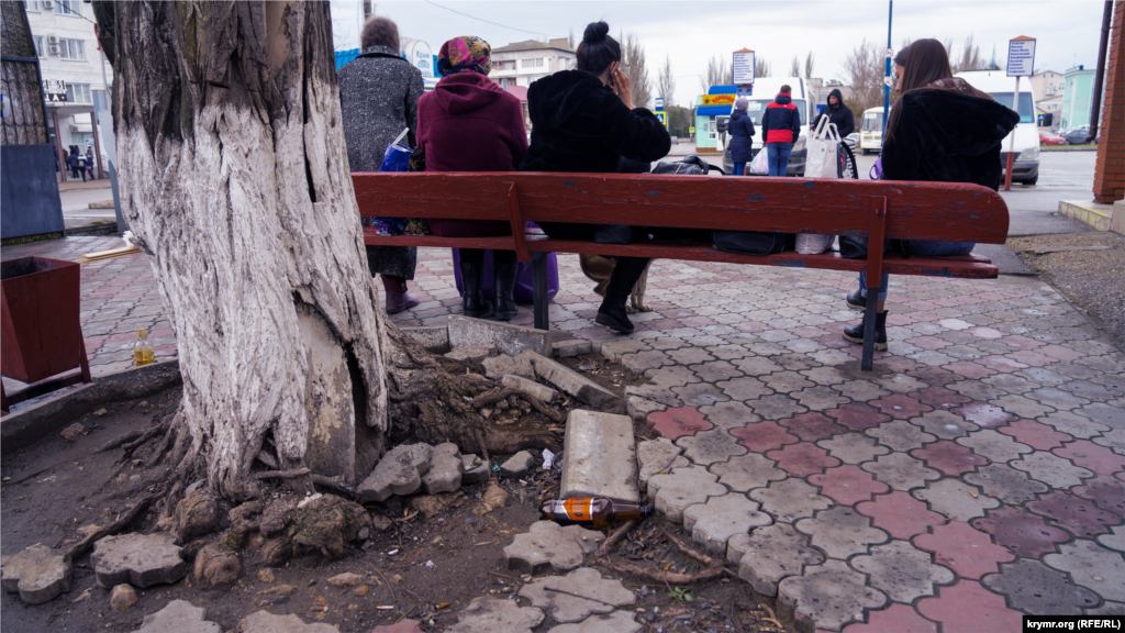 Пасажири на лавці біля будівлі автостанції, що на тій самій вулиці, поруч із залізничним вокзалом